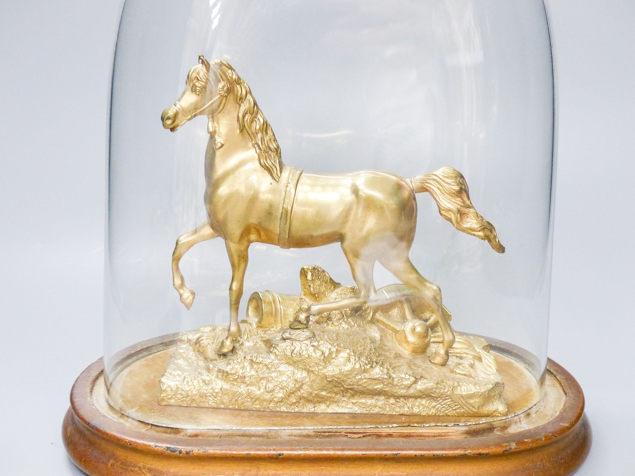 A Victorian gilt metal model of a horse with trophies of war to the base, under a glass dome, total height 30 cm